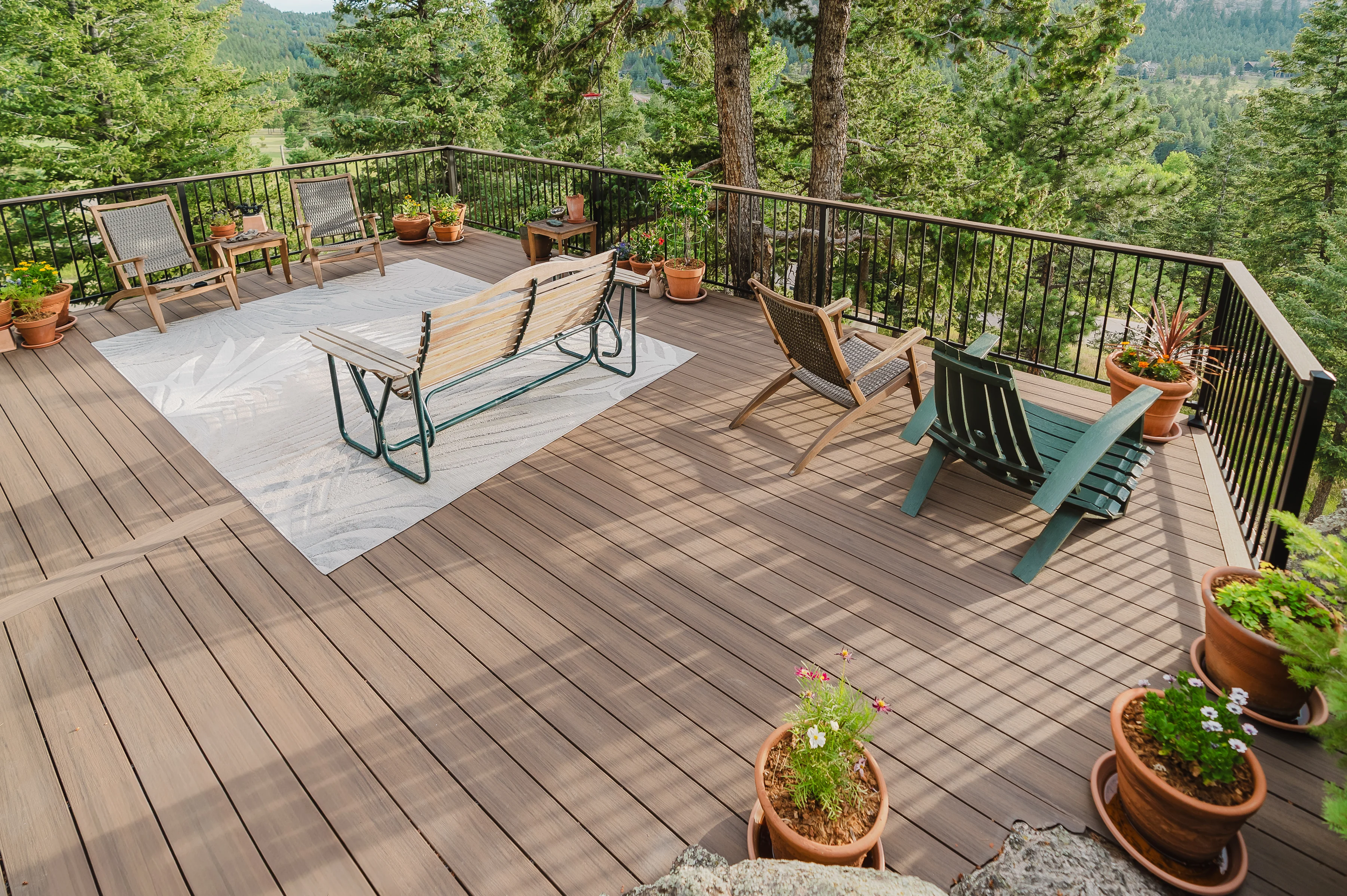 Spacious deck with dark metal railing, lounge chairs and potted flowers among tall pines